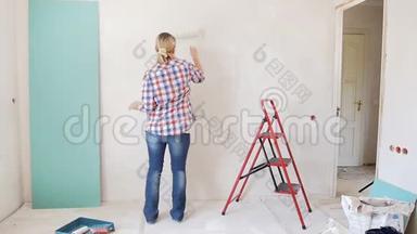 慢镜头的快乐年轻女子跳舞时，在她的公寓墙画。 年轻女孩正在装修